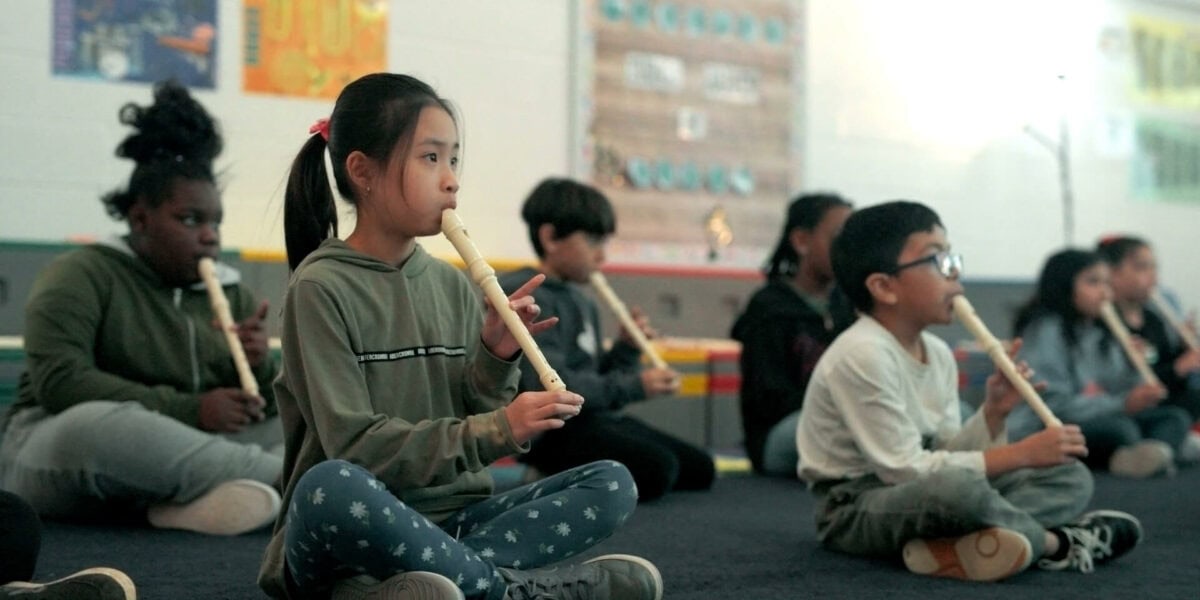Group of diverse young students playing recorders in music class