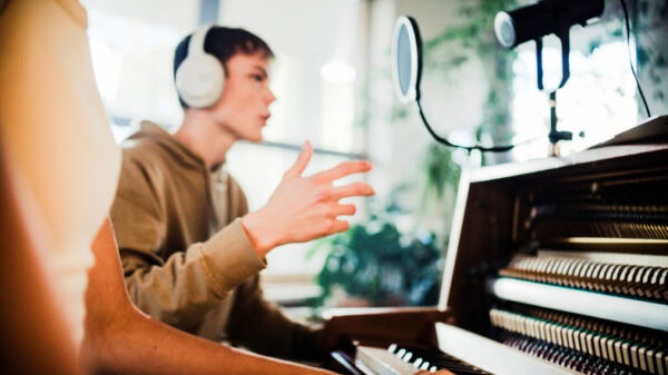 Male student wearing headphones practicing singing lessons and woman accompanying with rap background music on the piano